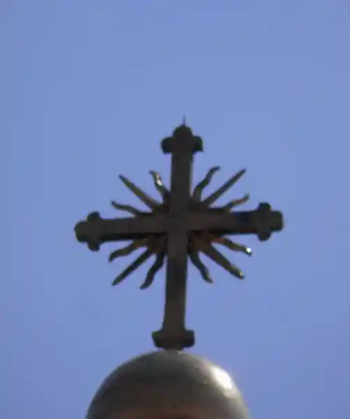 Cross with sun rays emitting from the center on top of a steeple